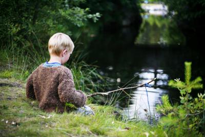 Lille dreng sidder ved en å og fisker med en hjemmelavet fiskestang