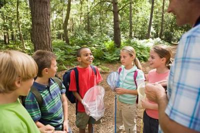På billedet ses 5 børn og en voksen, der taler sammen. I baggrunden er der skov. Solen skinner og det er sommer